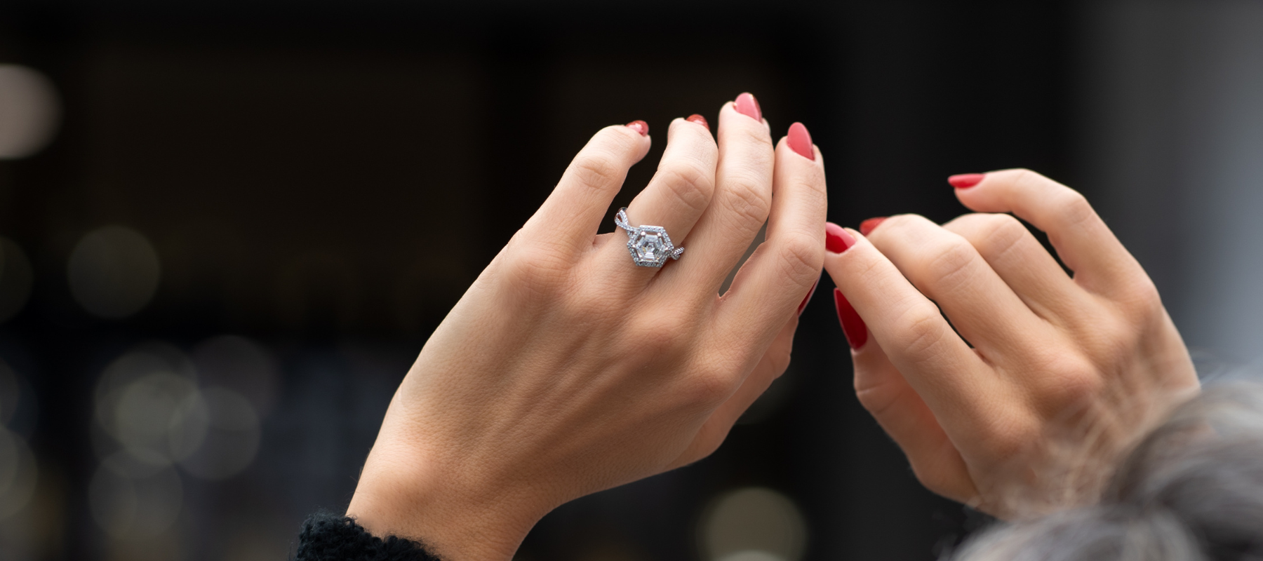 A beautiful diamond engagement ring on the left hand of a women with bright red nails